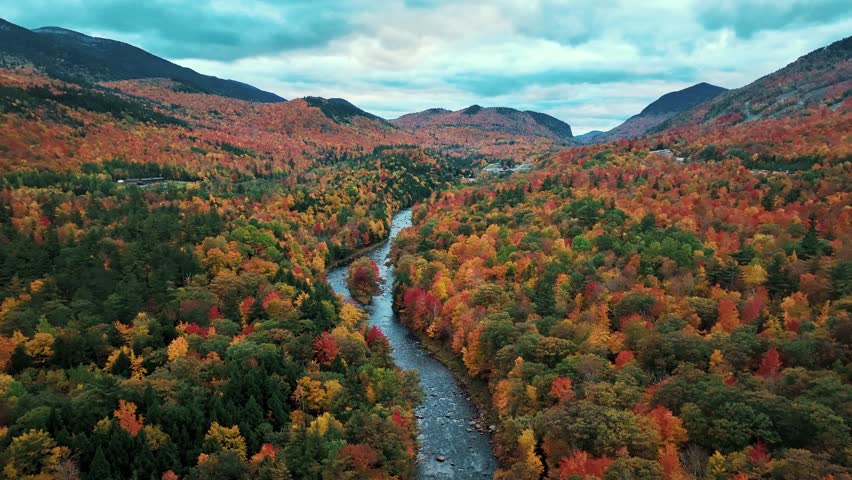 Adirondack Mountain, New York State. Aerial view of autumnal forest with river and mountains in the background, showcasing a vibrant palette of red, orange, yellow, and green.