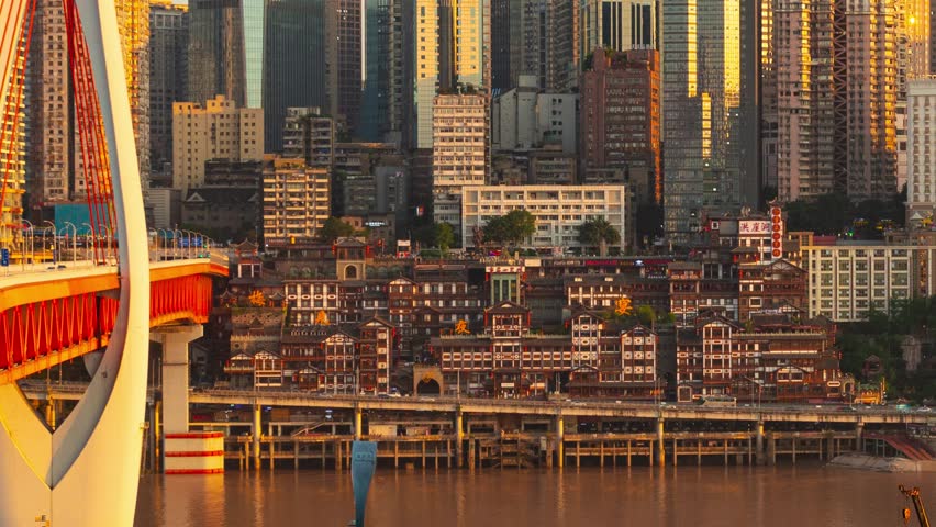 Chongqing, China. Aerial view of a cityscape during sunset with skyscrapers and a bridge in the foreground. The city skyline is illuminated by the setting or rising sun, casting a warm.