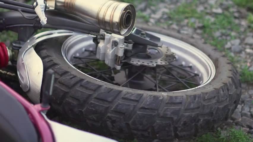 Closeup slow motion view of a motorcycle wheel lying on the ground after a crash, highlighting impact, debris, and the aftermath of an accident region