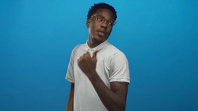 Man wearing white polo shirt and glasses casually points thumb backwards in studio against vibrant blue wall; confidence. - Powered by Shutterstock - Get 15% off with code: PIKWIZARD15