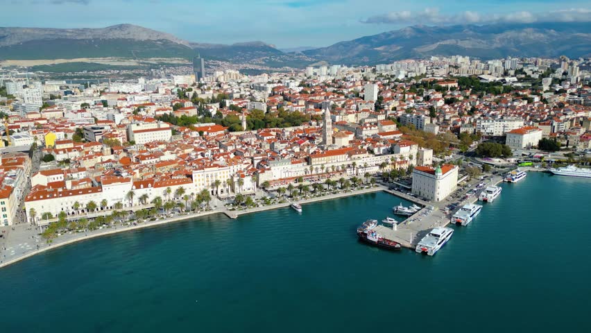 Aerial view of Split, Croatia, showcasing the historic city, Riva promenade, and bustling port against the backdrop of the Adriatic Sea and mountains. A vibrant Mediterranean scene.