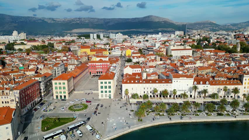 Aerial view of Split, Croatia, showcasing its vibrant harbor, historic red-roofed buildings, and lush Marjan Hill under a clear Adriatic sky. A perfect Mediterranean escape.
