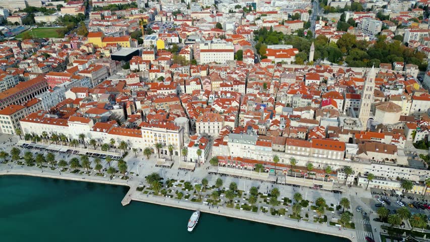 Aerial view of Split, Croatia, showcasing its historic core, bustling Riva promenade, and the Adriatic Sea backed by mountains under a clear autumn sky.