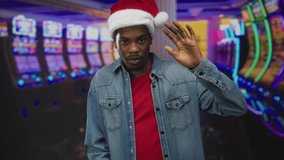 Man waves hand at slot machine in casino building wearing santa hat and denim jacket under neon lights; celebration. - Powered by Shutterstock - Get 15% off with code: PIKWIZARD15