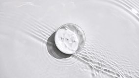 A jar of white cream on a water surface. Splash of water, sunlight and shadows. Layout for advertising goods, cosmetic products. Medical skin care, body care. - Powered by Shutterstock - Get 15% off with code: PIKWIZARD15