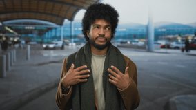 African american man with beard standing outdoors at airport looking puzzled wearing a scarf and coat under the modern structured roof. - Powered by Shutterstock - Get 15% off with code: PIKWIZARD15