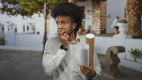 African american man holding blueprints on city street checks time looking at smartwatch. - Powered by Shutterstock - Get 15% off with code: PIKWIZARD15