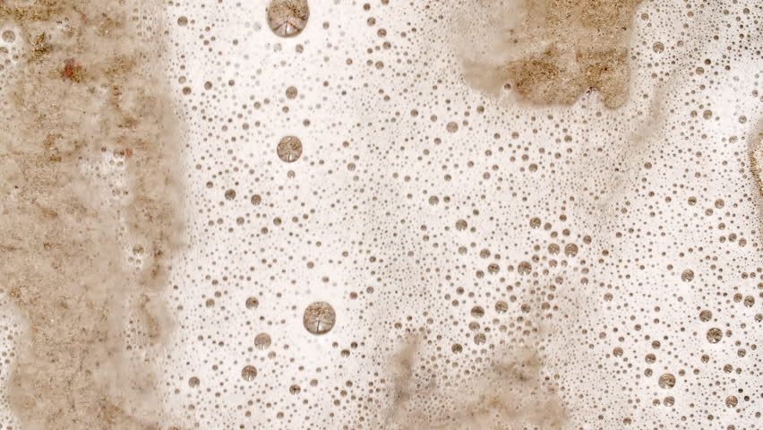 Waves of White Soapy Foam Flowing Down the Yellow Surface. Texture of Bubbles on abstract background. Soap sud macro structure. Bathtup Soap Foam. Natural White Shampoo Bubbles Motion.