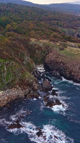 Sunrise casts a golden glow on jagged cliffs as waves crash onto rocky shores, creating a peaceful scene of nature