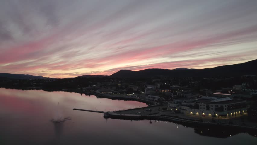 Minimalist drone shot of pink and red evening sky reflecting on a glassy fjord near Fauske, Norway. Subtle movement, gentle clouds, and quiet mountains create a calming nordic sunset scene.