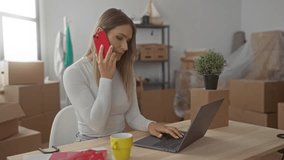 Young woman with blonde hair using a red phone and laptop in a new home surrounded by cardboard boxes and household items, implying a recent move or relocation. - Powered by Shutterstock - Get 15% off with code: PIKWIZARD15