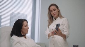 Cosmetic professional doctor in uniform reviewing skincare treatment options on smartphone with female client in bathrobe during professional medical aesthetic consultation in clinic, slow motion. - Powered by Shutterstock - Get 15% off with code: PIKWIZARD15