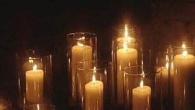 A group of lit ivory pillar candles in clear glass holders arranged closely together, casting a golden glow against a rustic brick wall background. - Powered by Shutterstock - Get 15% off with code: PIKWIZARD15