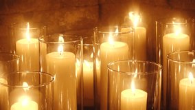 A group of lit ivory pillar candles in clear glass holders arranged closely together, casting a golden glow against a rustic brick wall background. - Powered by Shutterstock - Get 15% off with code: PIKWIZARD15