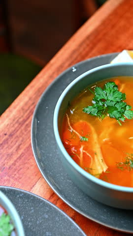 Chicken soup with herbs. Hot chicken soup with vegetables and herbs in a ceramic bowl.
