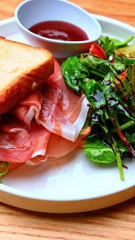 Salad and ham toast on plate. Light plate with toasted sandwich and mixed leafy greens drizzled.