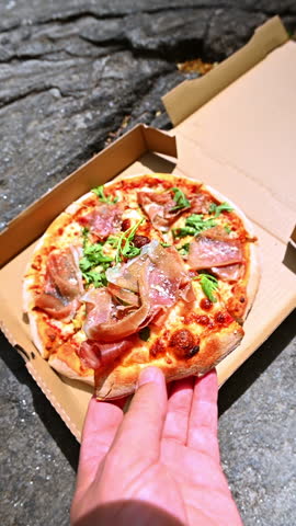 Hand taking slice of prosciutto pizza. A hand reaches for a prosciutto pizza slice during a relaxed park meal.