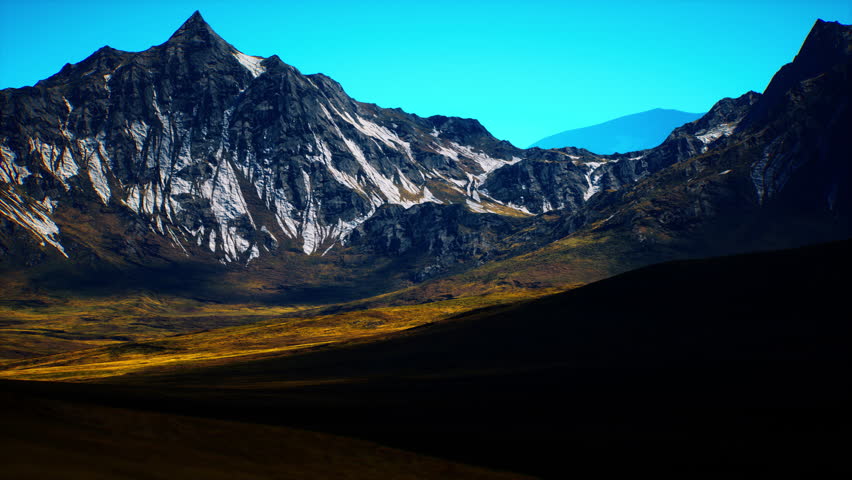 Giant mountains rise dramatically against a brilliant blue sky, showcasing rugged peaks and patches of snow. The golden light of dawn casts long shadows across the valley below.