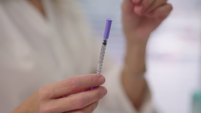 Close-up hands of unrecognizable cosmetologist holding medical syringe with fine needle, preparing for cosmetic injection or medical treatment. Concept of health, beauty, pharmaceutical applications.