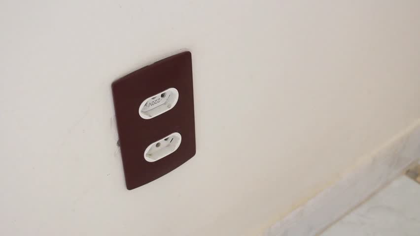 Female hand using a voltage tester pen to detect electricity in a wall socket. The tester lights up when approaching an energized power outlet. Horizontal video ideal for electrical inspection.