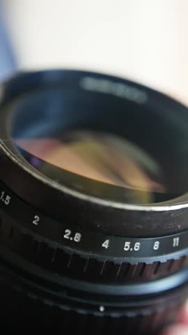 aperture markings on lens, studio lighting highlights glass reflections and tactile metal surface, closeup view of classic camera lens with aperture and focus adjustments in warm lighting