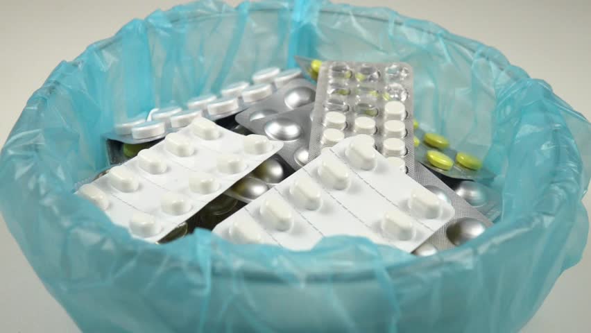 Various expired pills pour into a container with expired pill blister packs, rotation. Medicines background,  top view, slow motion