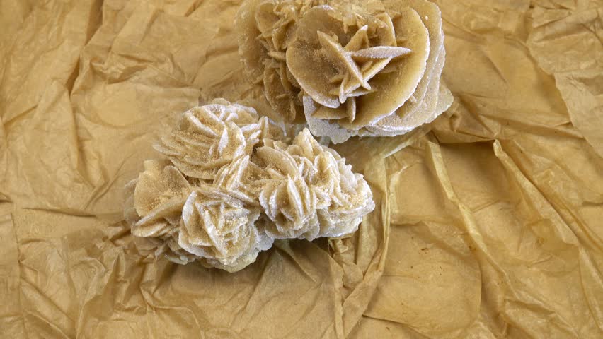 Stone sand rose is rotating against the beige textured background from handmade craft paper, stone illumination, rotation