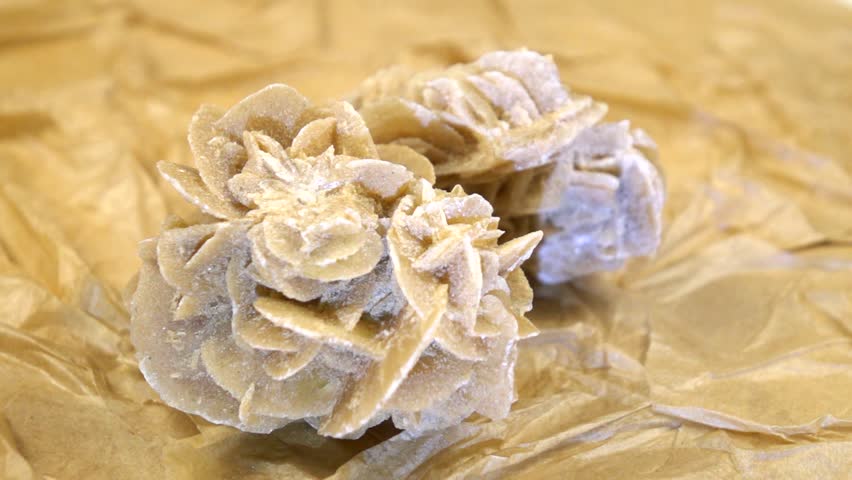 Stone sand rose is rotating against the beige textured background from handmade craft paper, stone illumination, slow motion