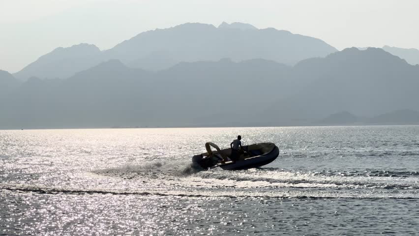 Two people riding a banana boat being pulled by a speedboat near the beach with mountains in the background