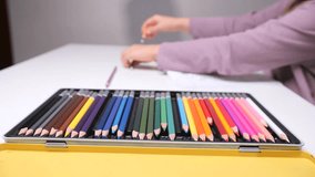 Childs hand reaching for a colorful pencil from an open metal case, engaging in creative activities like drawing, coloring, and learning art at a table - Powered by Shutterstock - Get 15% off with code: PIKWIZARD15