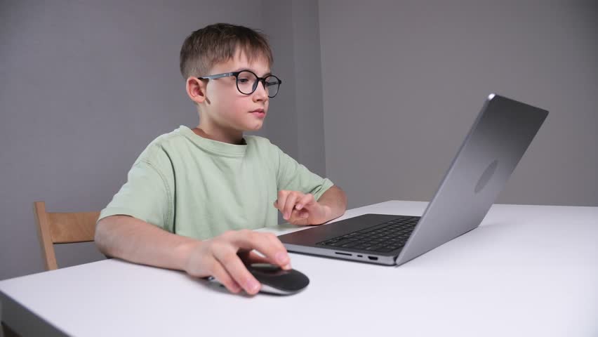 Young bespectacled boy concentrating and actively engaging with a laptop computer while sitting at a desk, practicing digital skills and online education