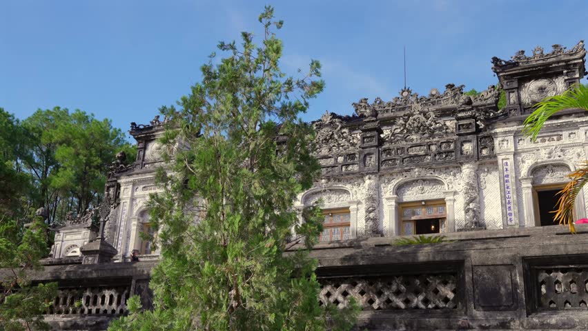 Intricate grey stone dragons and carvings adorn the majestic facade of Khai Dinh Mausoleum under a clear blue sky.