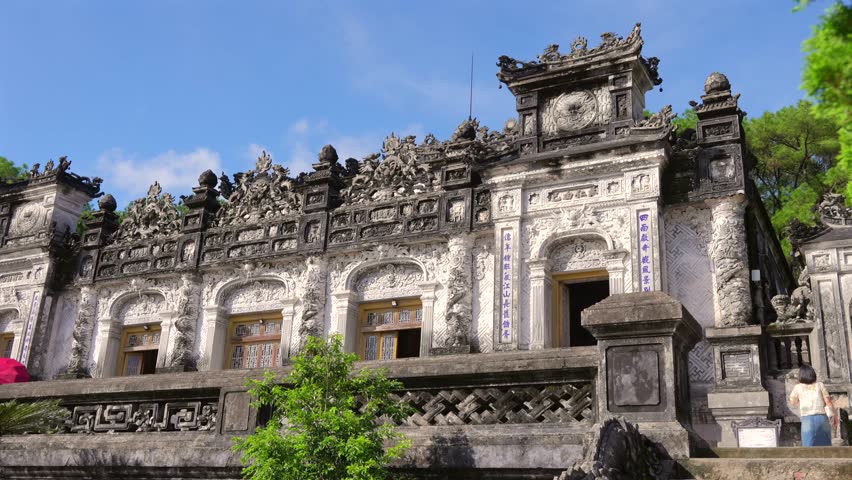 Intricate grey stone dragons and carvings adorn the majestic facade of Khai Dinh Mausoleum under a clear blue sky.
