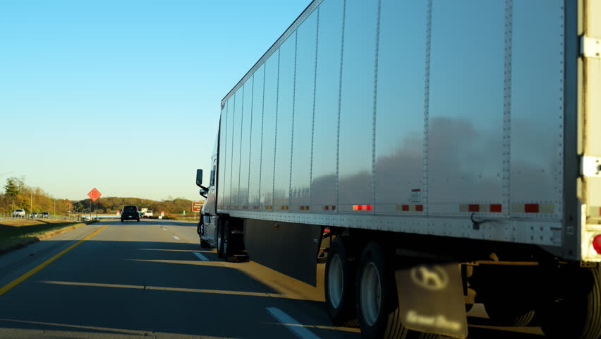 Semi truck hauling cargo along a busy interstate highway on a clear fall day. The trailer moves steadily through traffic, long haul trucking, logistics, supply chain operations