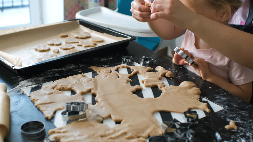A mother and her young daughter cut ginger cookie dough and place the shaped pieces onto a baking tray. Family lifestyle and home baking concept