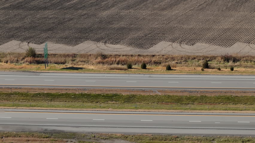 Multiple semi-trucks and cars traveling along a busy highway surrounded by flat plowed agricultural fields. The clip shows long-haul transportation, logistics, and supply chain