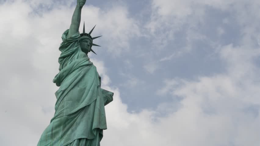 Statue of Liberty on Liberty Island, New York, United States. Blue cooper monument, symbol of democracy and patriotism near Manhattan, NYC USA. Clouds on sky. American independence. Torch and crown.