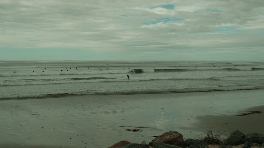 Surfers floating in water and catching waves in Tourmaline beach on a cloudy gloomy day