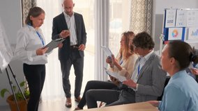 Group of business professionals participating in an office meeting. Female manager reads from clipboard, male executive holds smartphone, team listens attentively with documents. Concept of teamwork. - Powered by Shutterstock - Get 15% off with code: PIKWIZARD15