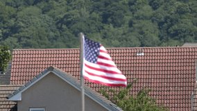 American flag flutters briskly above residential rooftops, daylight, static camera, lush green background - Powered by Shutterstock - Get 15% off with code: PIKWIZARD15