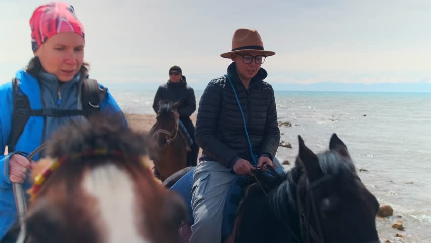 riders with horses along rocky coastal shoreline, two individuals on horseback capturing candid seaside moments, caucasian riders posing with horses on rocky coast with breezy ocean backdrop