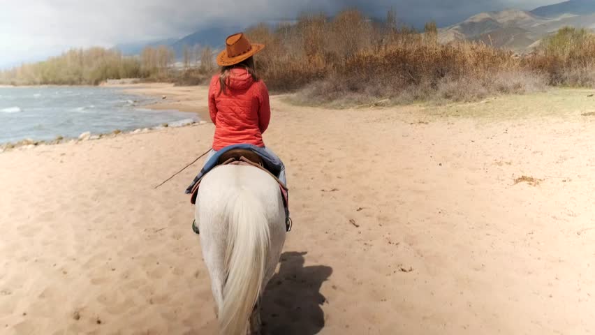 caucasian rider sharing peaceful riverbank journey, single rider leads guest along tranquil river with reeds and hills, quiet trail ride with guest beside rider through riverbank reeds and distant