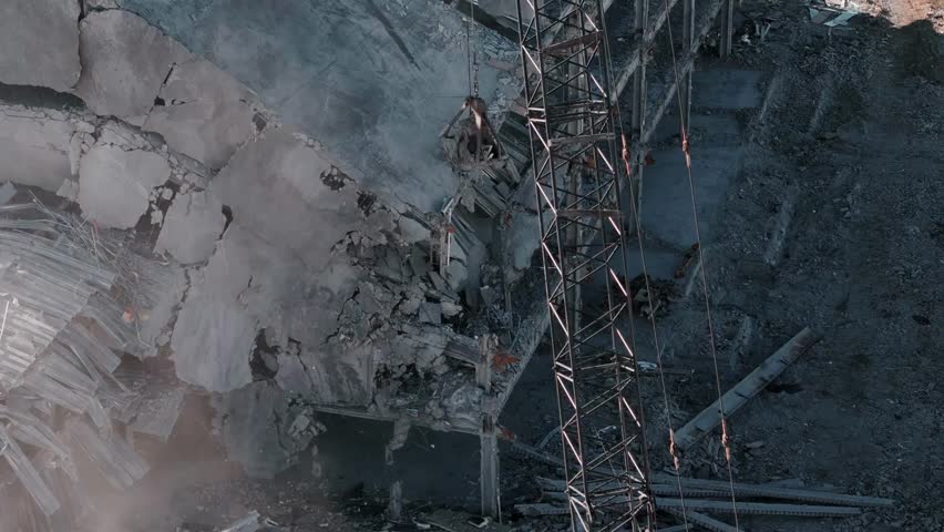 Aerial top-down view of buildings being demolished, capturing destruction, dust, and debris in an urban demolition site.