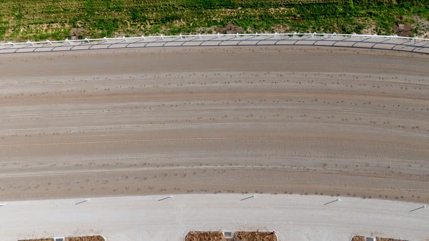 Aerial top-down view of horses trotting on a Milan racecourse, captured by drone, showing motion, track layout, and equestrian action from above, slow motion drone