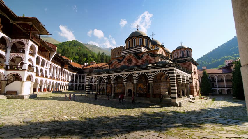 Exterior view of Rila Monastery in Bulgaria, sliding from the full building to a column, highlighting its historic architecture, stone details, and scenic mountain surroundings