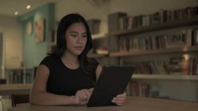Beautiful Asian Thai woman in library using digital tablet computer looking surprised and shocked - Powered by Shutterstock - Get 15% off with code: PIKWIZARD15