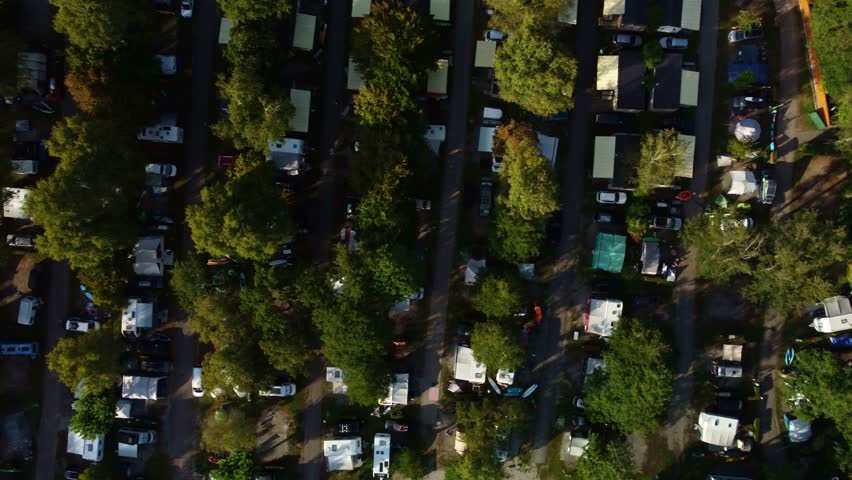 Top down view of a campsite in France. Lac Bleu and the bottom end of Lake Annecy. Drone footages moves to left showing the lines of tents and camper vans separated with paths and lines of trees.