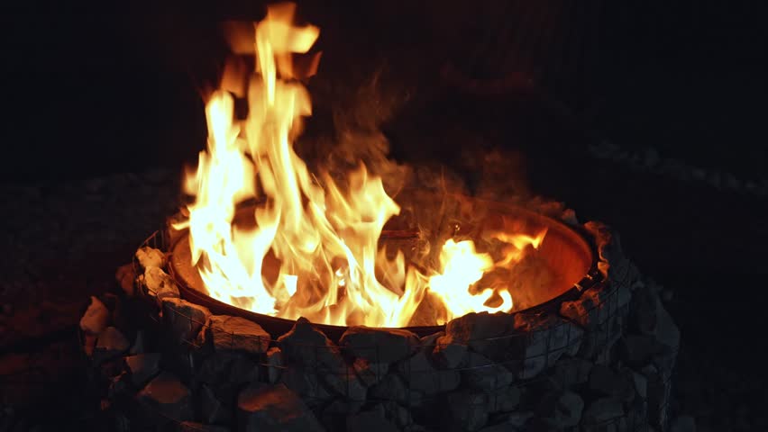 Night stone fire pit glowing, gentle flames lap stone ring and embers drift upward, warm orange glow, soft crackle and smoke, meditative outdoor atmosphere ideal for relaxation and evening