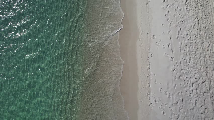 Emerald Gulf of Mexico aerial drone shot, focusing directly down on crystal clear turquoise water washing over pristine white sand beach.