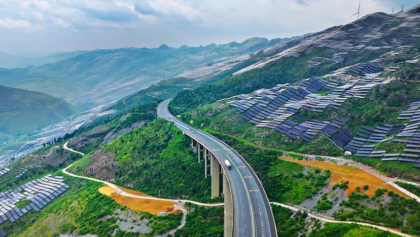  Aerial shot of highway bridge winding through green mountains covered with solar panels energy farm in China